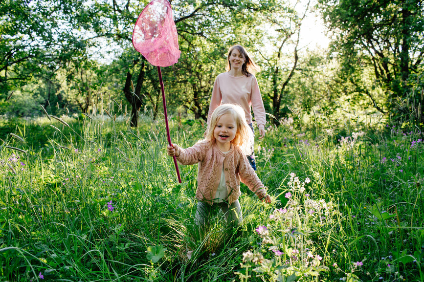 Young girl and her mom playing in a field with a butterfly net